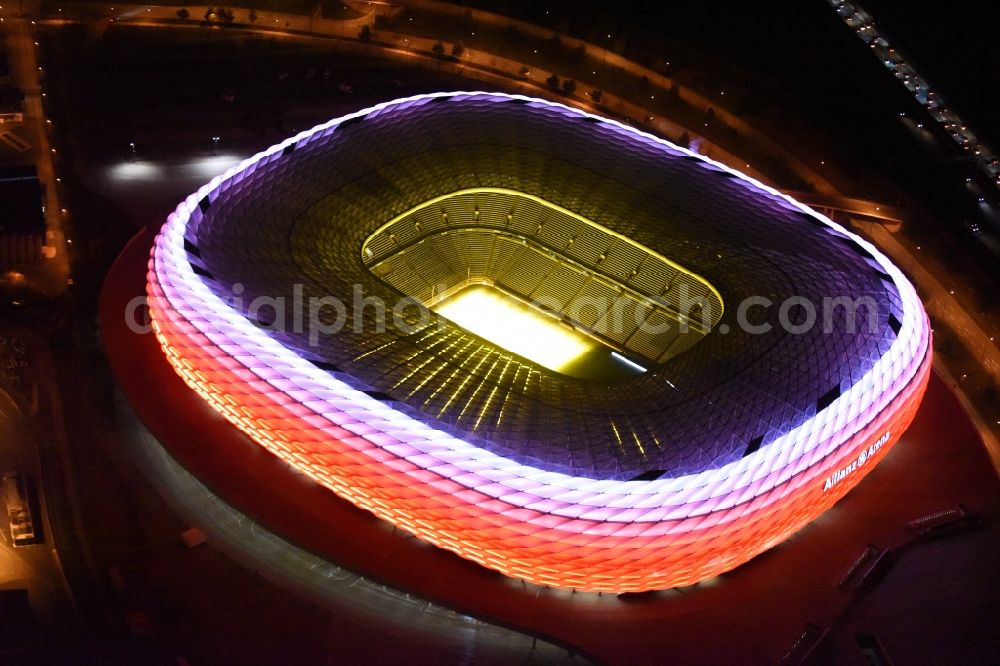 München at night from the bird perspective: Night lighting the Allianz Arena in Munich in Bavaria is a football stadium of the the Munich football club FC Bayern Muenchen. The facade of the, designed by the architects Herzog & de Meuron stadium Allianz Arena Muenchen Stadion GmbH consists of illuminated white foil cushions