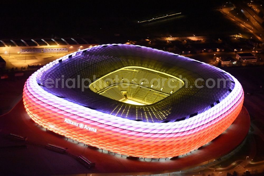 Aerial photograph at night München - Night lighting the Allianz Arena in Munich in Bavaria is a football stadium of the the Munich football club FC Bayern Muenchen. The facade of the, designed by the architects Herzog & de Meuron stadium Allianz Arena Muenchen Stadion GmbH consists of illuminated white foil cushions