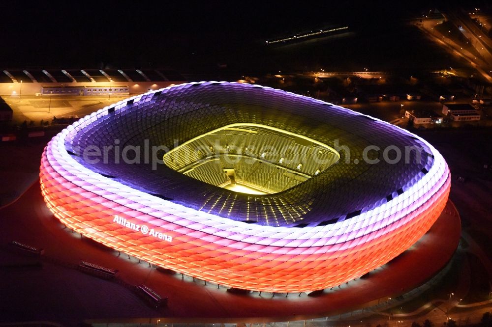 Aerial image at night München - Night lighting the Allianz Arena in Munich in Bavaria is a football stadium of the the Munich football club FC Bayern Muenchen. The facade of the, designed by the architects Herzog & de Meuron stadium Allianz Arena Muenchen Stadion GmbH consists of illuminated white foil cushions
