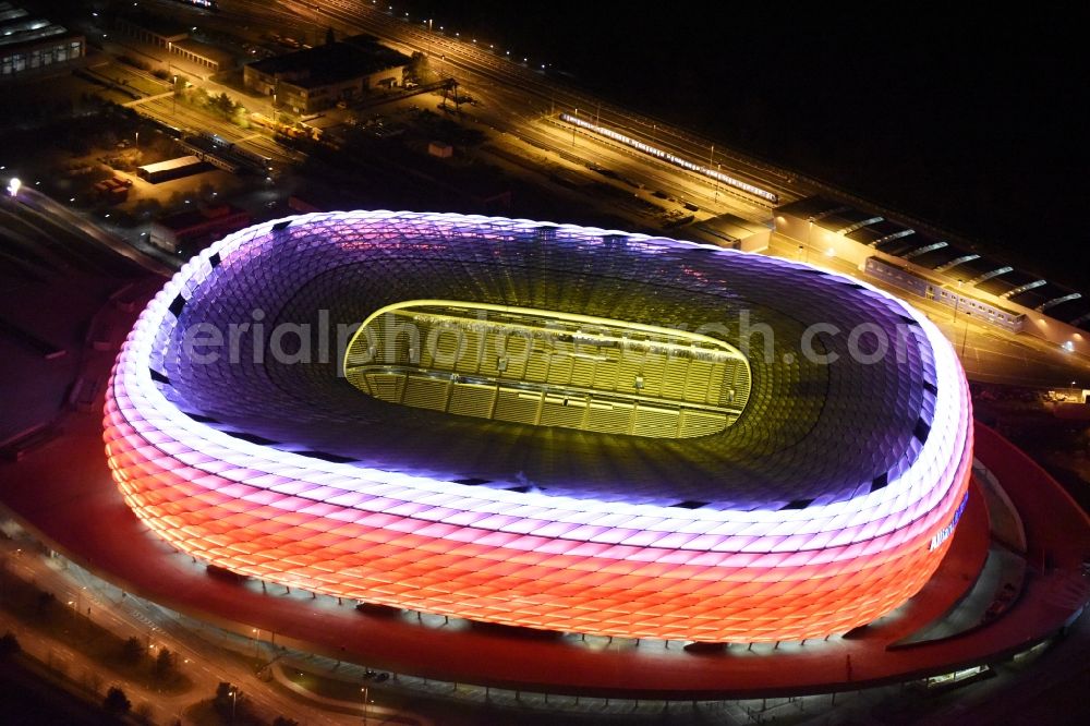 München at night from the bird perspective: Night lighting the Allianz Arena in Munich in Bavaria is a football stadium of the the Munich football club FC Bayern Muenchen. The facade of the, designed by the architects Herzog & de Meuron stadium Allianz Arena Muenchen Stadion GmbH consists of illuminated white foil cushions