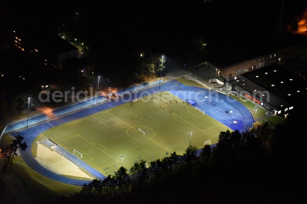 Aerial image at night Kleinmachnow - Night image of the sports facilities of the Berlin Brandenburg International School and residential buildings in Kleinmachnow in the state of Brandenburg. The BBIS includes a football pitch and athletics facilities in a distinct blue colour. Residential buildings and estates as well as a primary school are surrounded by trees and woods