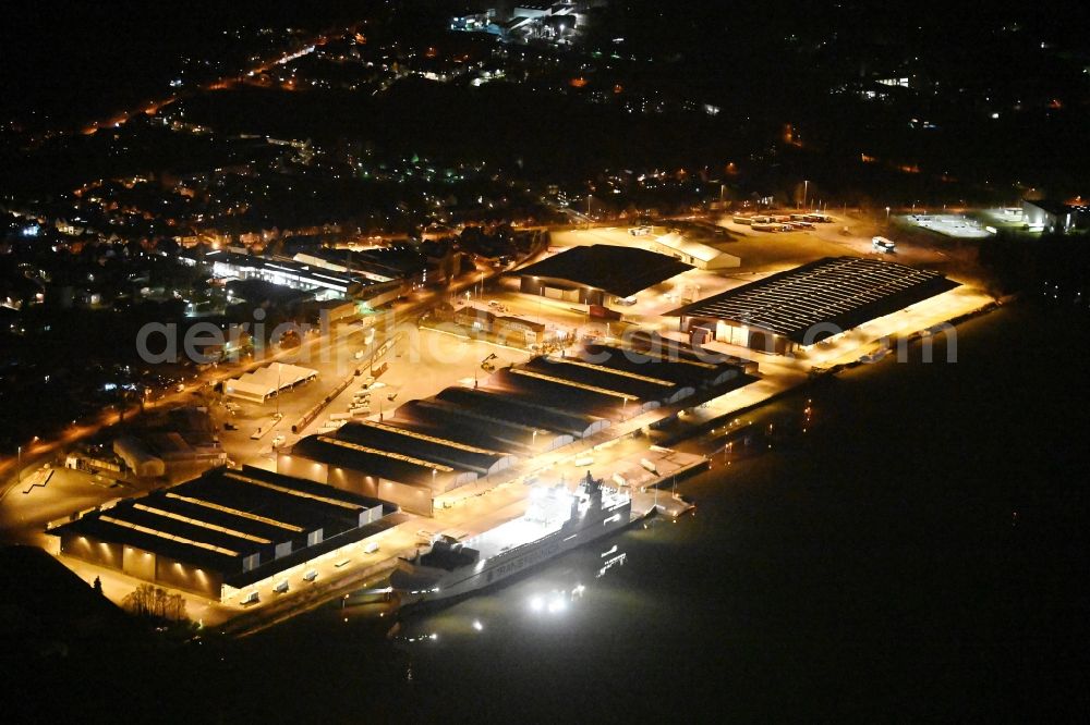 Aerial image at night Lübeck - Night lighting warehouse complex-building in the industrial area on the banks of the River Trave at Fabrikstrasse overlooking an anchored cargo ship in Luebeck in the state Schleswig-Holstein