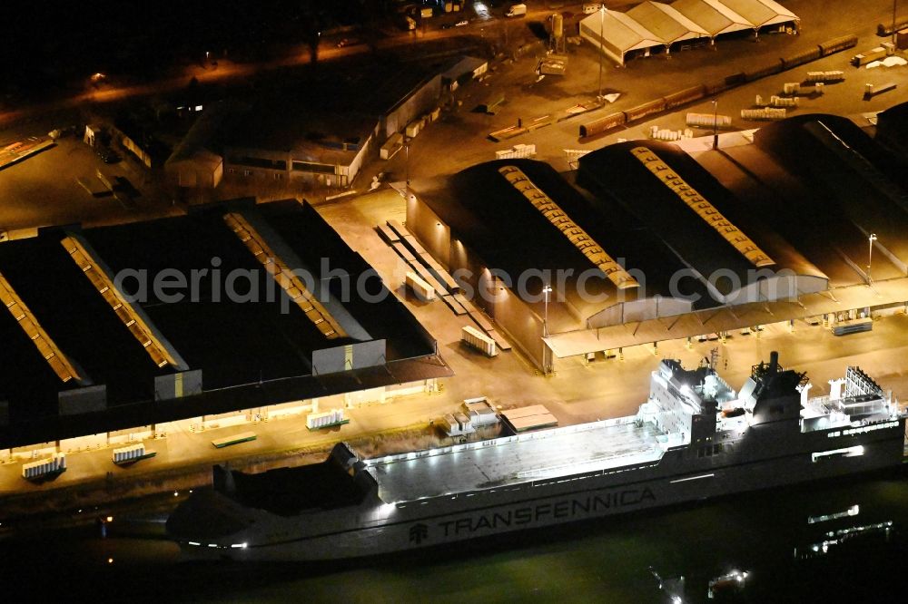 Lübeck at night from the bird perspective: Night lighting warehouse complex-building in the industrial area on the banks of the River Trave at Fabrikstrasse overlooking an anchored cargo ship in Luebeck in the state Schleswig-Holstein