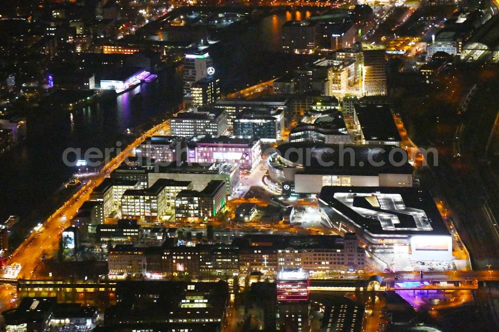 Aerial photograph at night Berlin - Night lighting Arena Mercedes-Benz-Arena on Friedrichshain part of Berlin. The former O2 World - now Mercedes-Benz-Arena - is located in the Anschutz Areal, a business and office space on the riverbank
