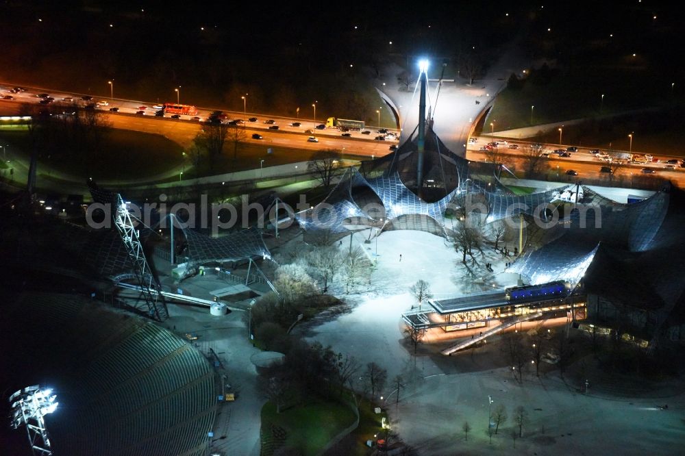 München at night from the bird perspective: Night Aerial view of building the Olympic Hall in Olympic Park at Georg-Brauchle-Ring in Munich in Bavaria. In the foreground the Restaurant Olympia Park beer garden right on Coubertinplatz