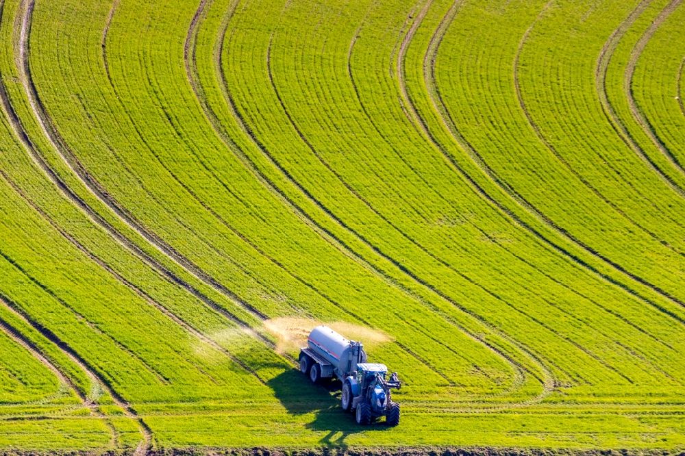 Enkhausen from above - Spraying manure as fertilizer with tractor and tank trailer on agricultural fields in Enkhausen in the state North Rhine-Westphalia, Germany