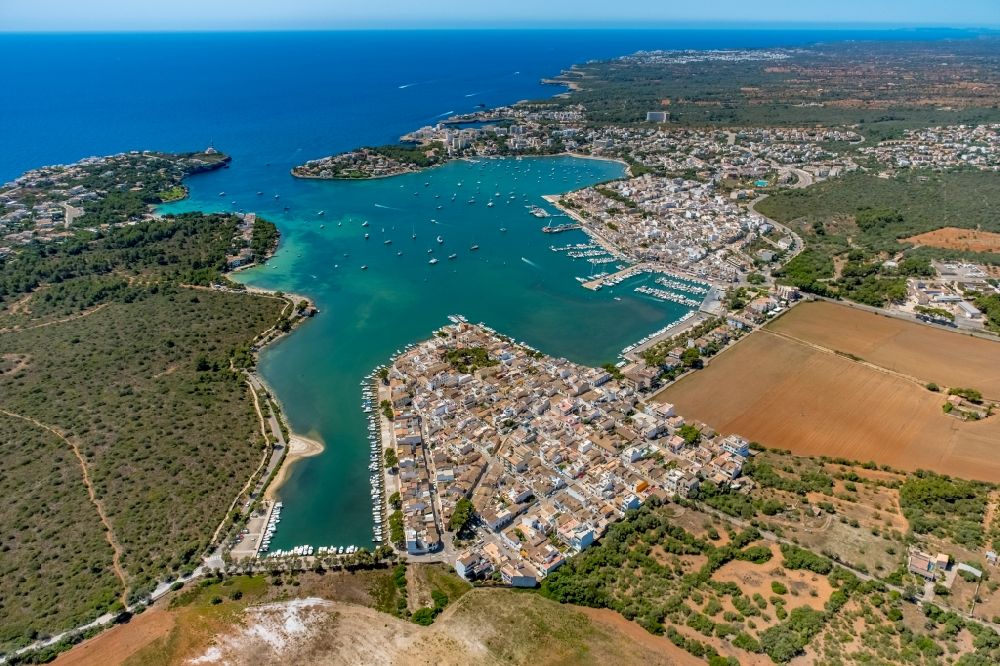 Aerial image Portocolom - Water surface at the bay along the sea coast overlooking the town and the port facilities of Port de Portocolom in Portocolom in Balearic islands, Spain