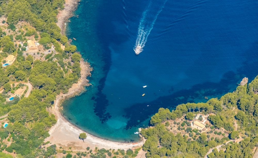 Aerial image Escorca - Water surface at the bay along the sea coast with a motorboat in motion at the beach of the Platja Tuent in Cala Tuent in Balearic island of Mallorca, Spain