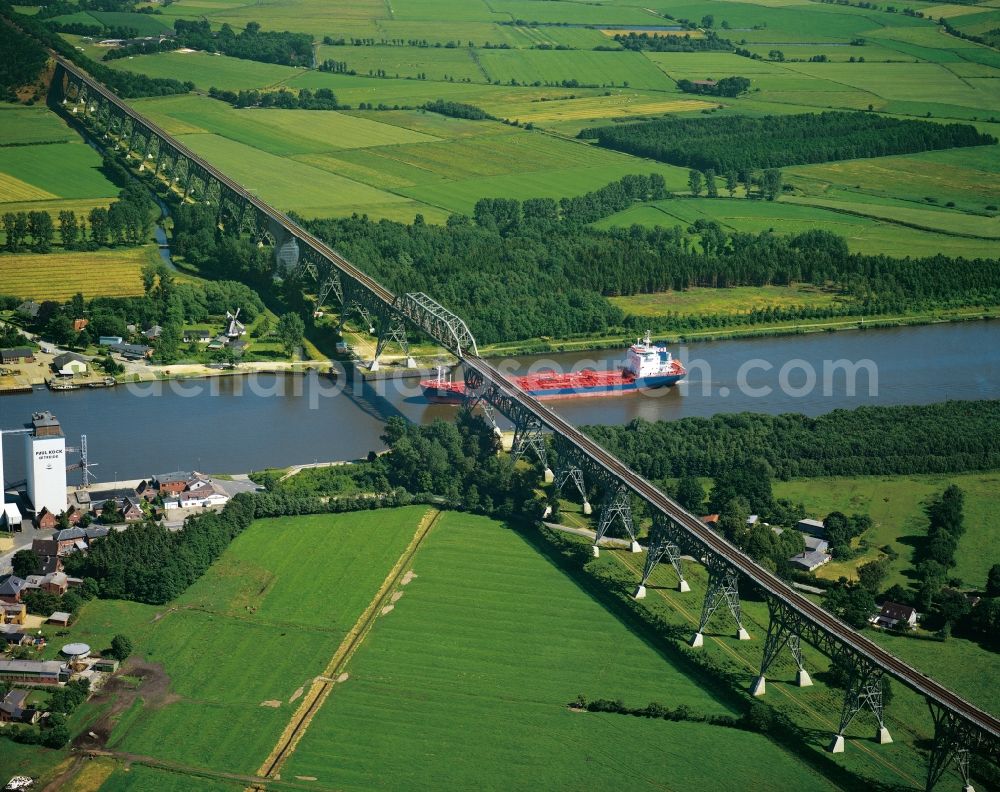 Aerial photograph Burg - The North-East Sea Channel in Dithmarschen in the state of Schleswig-Holstein. The channel is the most used artificial water way in the world. It runs throught the landscape which is mostly informed by fields and is used by various ships. View of the railway bridge in Burg