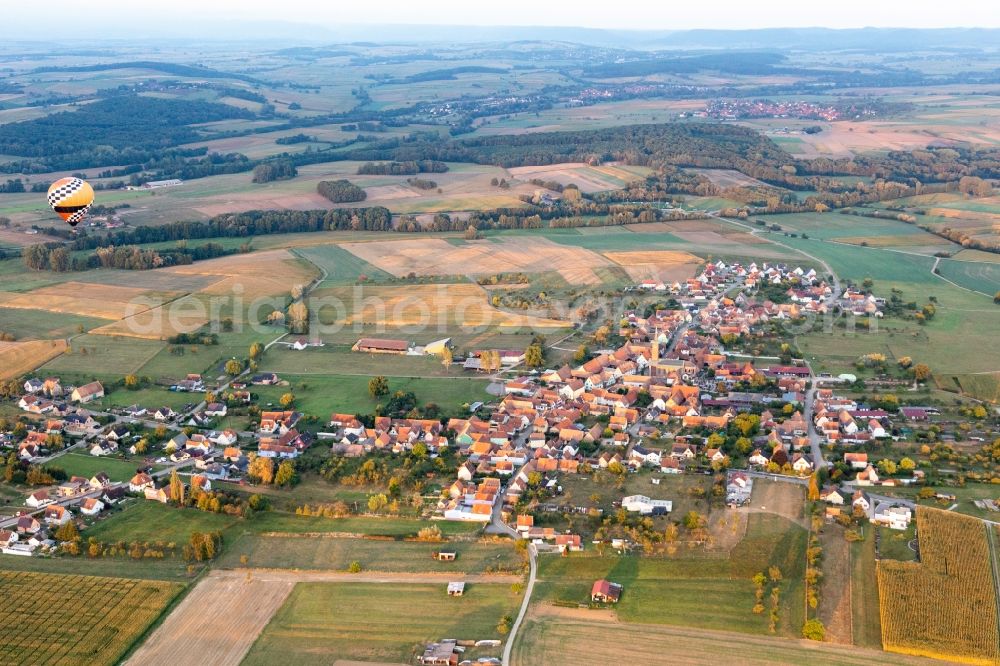 Kindwiller from the bird's eye view: Agricultural land and field borders surround the settlement area of the village with hot air ballon in Kindwiller in Grand Est, France