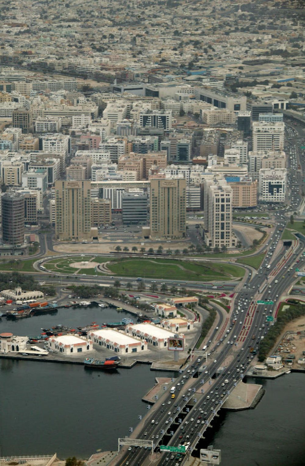 Dubai from above - Die Al Maktoum Brücke führt über den Dubai Creek. Der Dubai Creek ist ein natürlicher Meeresraum des Persischen Golfs, welcher die Stadt Dubai in die Stadtteile Bur Dubai und Deira teilt. Er ist 14 Kilometer lang und hat eine Breite von 115 Metern an der Mündung bis zu 1400 Metern an seinem Ende. Der Creek war einst das Zentrum der Stadt und der wichtigste Hafen. Im Vordergrund ist links das Hilton zu sehen. Die Al Maktoum Bridge ist e?