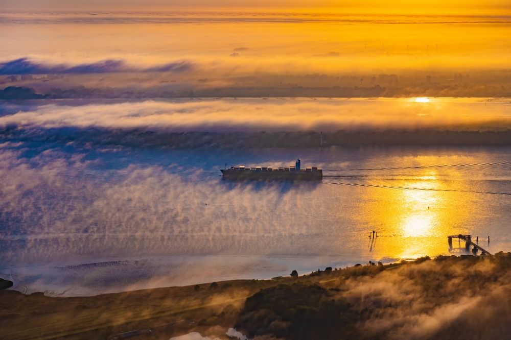 Kollmar from the bird's eye view: Voyage of a container ship of the SEASPAN DALIAN IMO: 9227027 in a layer of fog at sunrise on the course of the Elbe river in Kolmar in the state Schleswig-Holstein, Germany