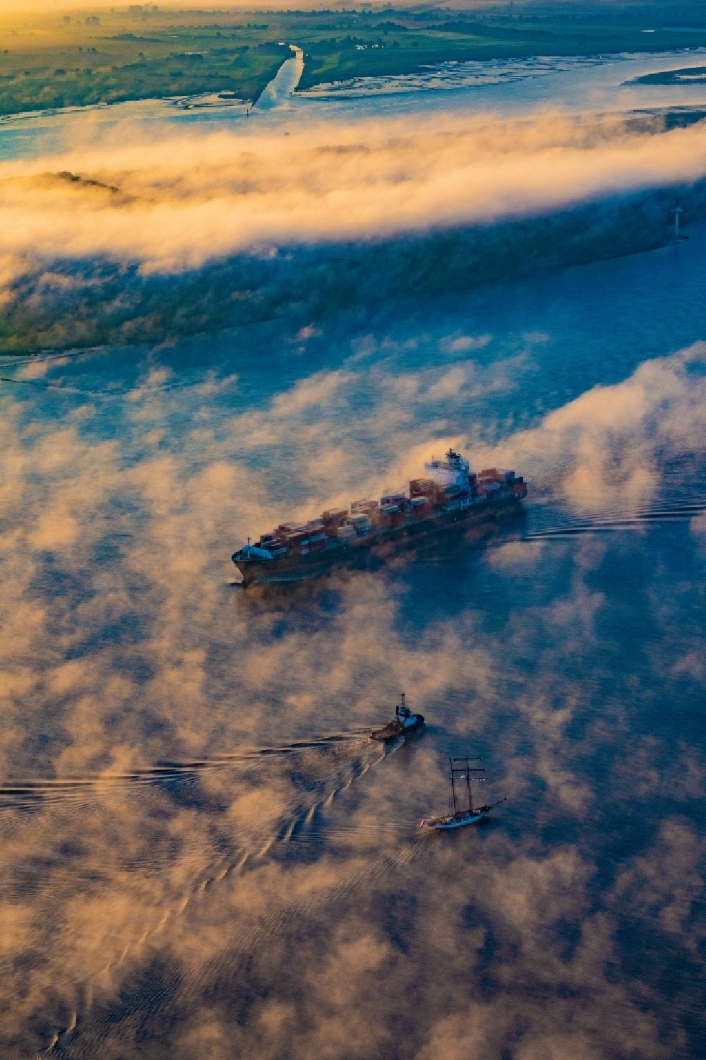 Kollmar from above - Voyage of a container ship of the SEASPAN DALIAN IMO: 9227027 in a layer of fog at sunrise on the course of the Elbe river in Kolmar in the state Schleswig-Holstein, Germany