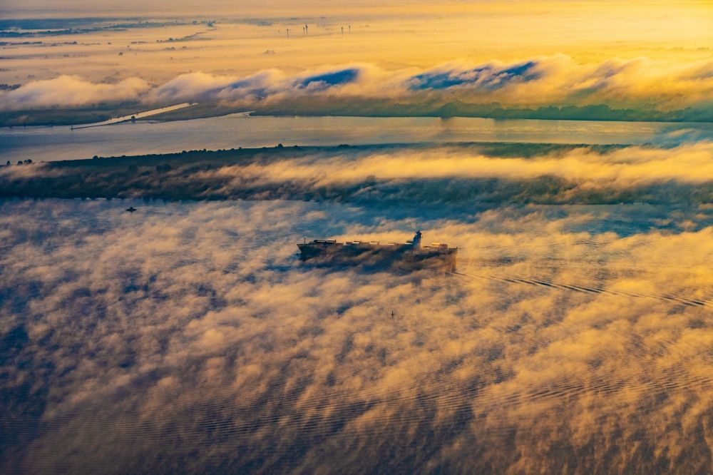 Kollmar from the bird's eye view: Voyage of a container ship of the SEASPAN DALIAN IMO: 9227027 in a layer of fog at sunrise on the course of the Elbe river in Kolmar in the state Schleswig-Holstein, Germany