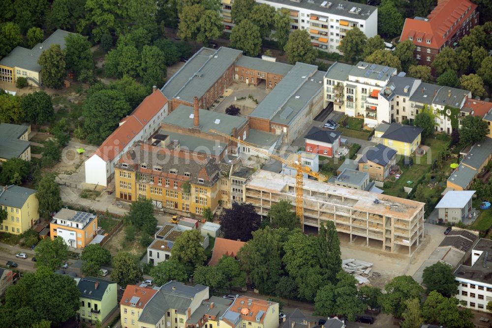 Aerial image Berlin - Historic factory and construction site of a new development amidst a residential area in the Friedrichshagen part of Berlin in Germany. The area is located between Ahornallee and Peter-Hille-Strasse and includes single and multi-family houses as well as the factory with the yellow main building and halls with a chimney. A construction site of a new development is sitting next to it