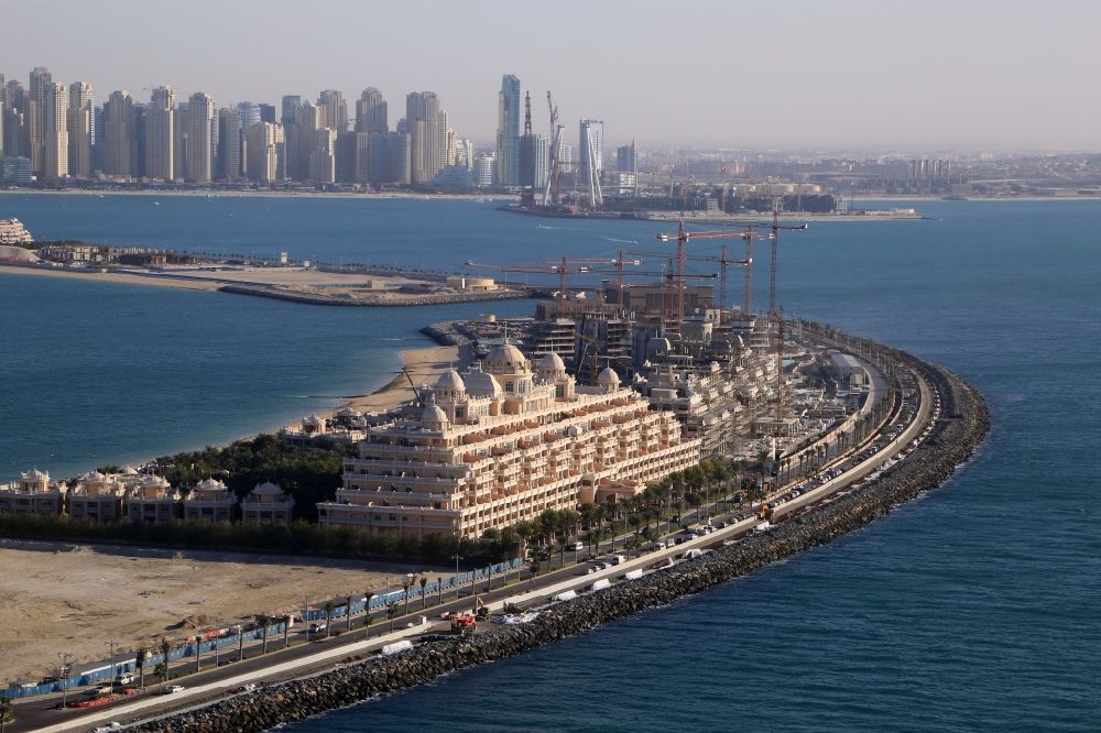 Aerial image Dubai - Kempinski Hotel on the crescent of the Palm Island in Dubai in United Arab Emirates. In the background the skyline with skyscrapers of Dubai Marina