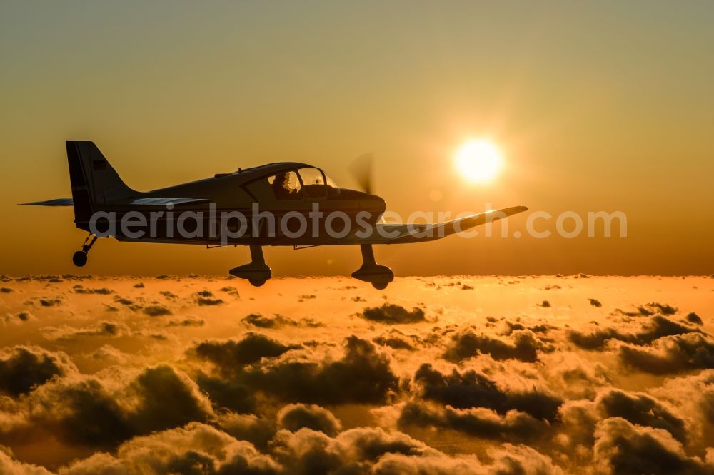 Cuxhaven from the bird's eye view: Motor aircraft and sports aircraft flying above clouds in the evening light of sunset over the airspace in Cuxhaven in the federal state of Lower Saxony, Germany