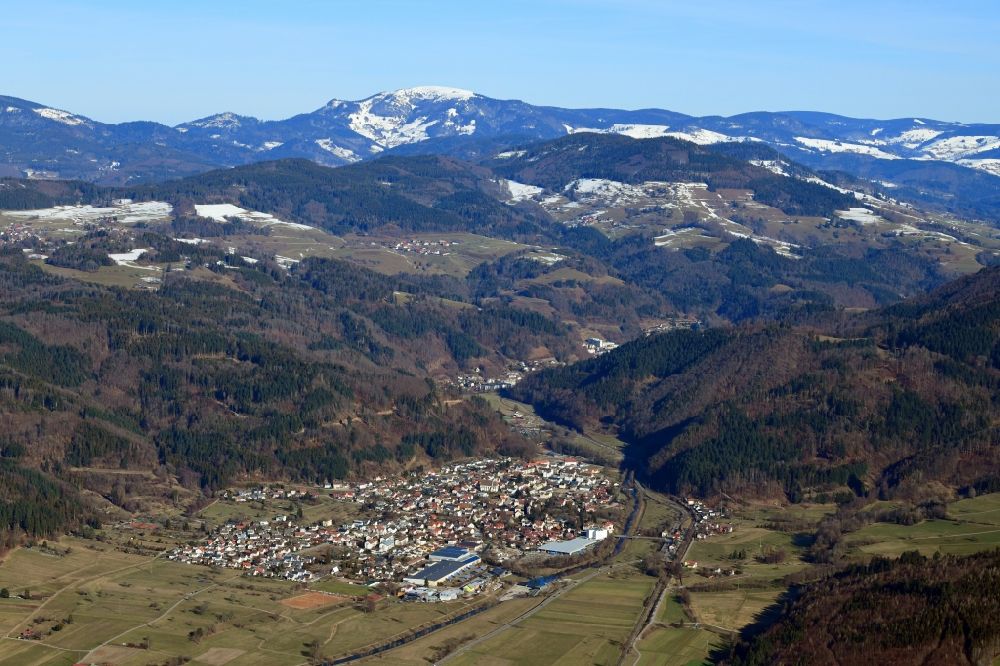 Hausen im Wiesental from the bird's eye view: Location view of residential areas in the valley landscape surrounded by mountains in Hausen im Wiesental in the state Baden-Wurttemberg, Germany. The bald summit of the Belchen in the Black Forest is still snow covered