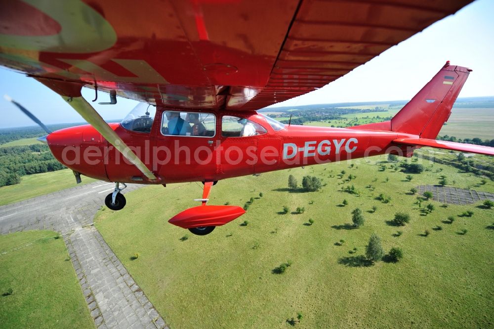 Werneuchen from the bird's eye view: Bright red Cessna 172 D-EGYC of the agency euroluftbild.de in flight over the airfield in Werneuchen in the state Brandenburg, Germany