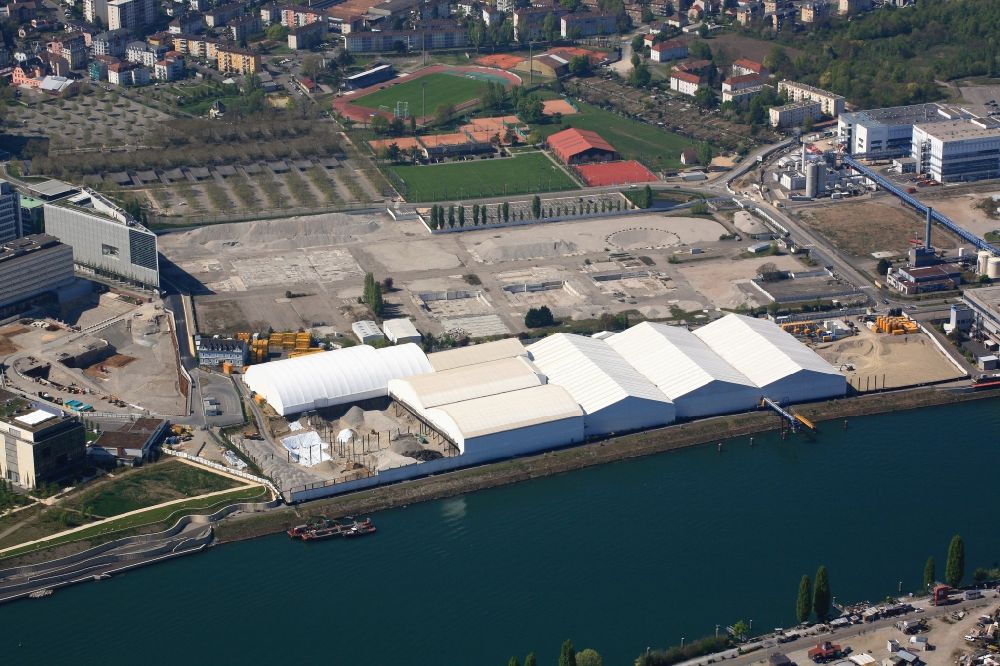 Aerial image Huningue - Directly on the border to Switzerland the pharmaceutical company Novartis in Huningue in France rehabilitates the site of former industrial wastewater treatment plant ARA Steih. The restoration work is carried out under tents to prevent odors and dust contamination. The excavation of contaminated material is transported by ship on the Rhine