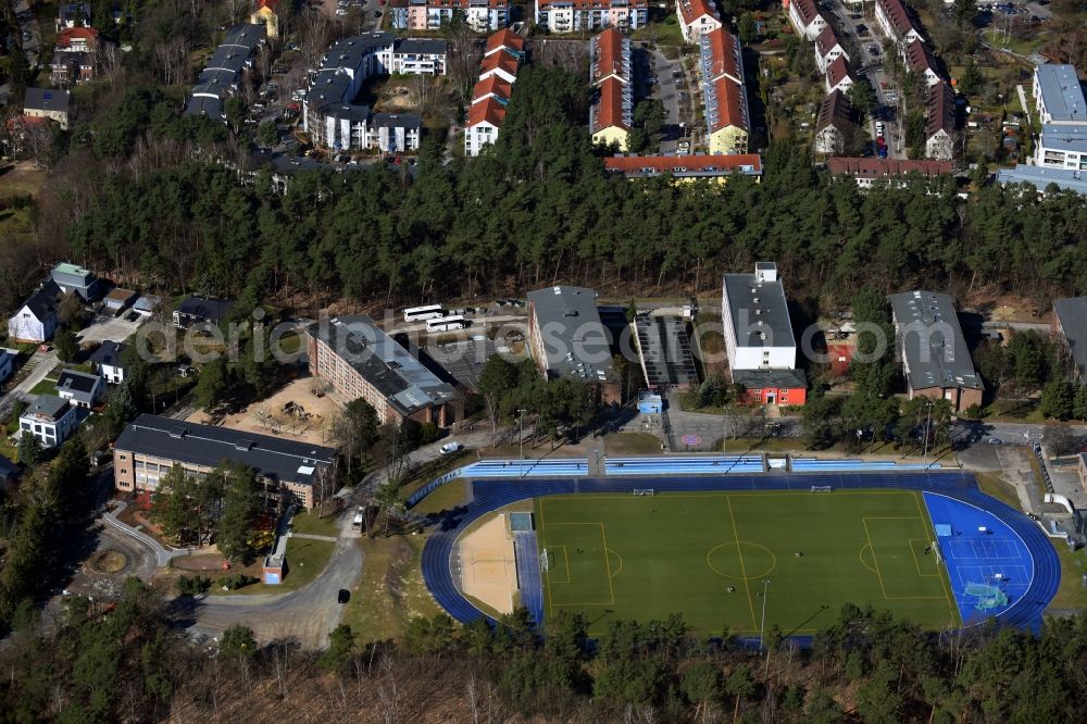 Aerial photograph Kleinmachnow - Sports facilities of the Berlin Brandenburg International School and residential buildings in Kleinmachnow in the state of Brandenburg. The BBIS includes a football pitch and athletics facilities in a distinct blue colour. Residential buildings and estates as well as a primary school are surrounded by trees and woods
