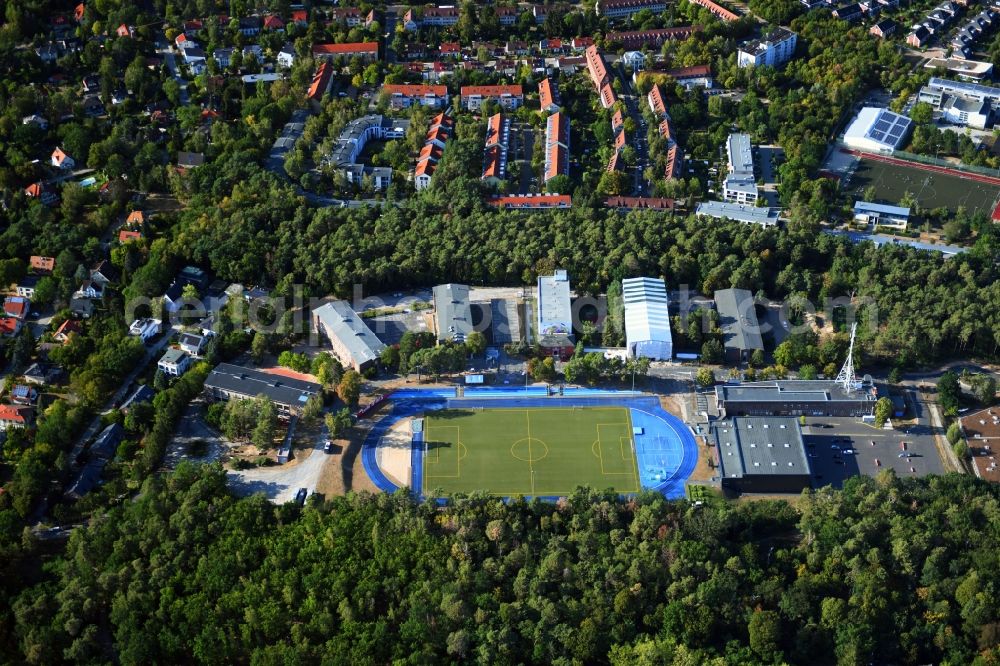 Kleinmachnow from the bird's eye view: Sports facilities of the Berlin Brandenburg International School and residential buildings in Kleinmachnow in the state of Brandenburg. The BBIS includes a football pitch and athletics facilities in a distinct blue colour. Residential buildings and estates as well as a primary school are surrounded by trees and woods