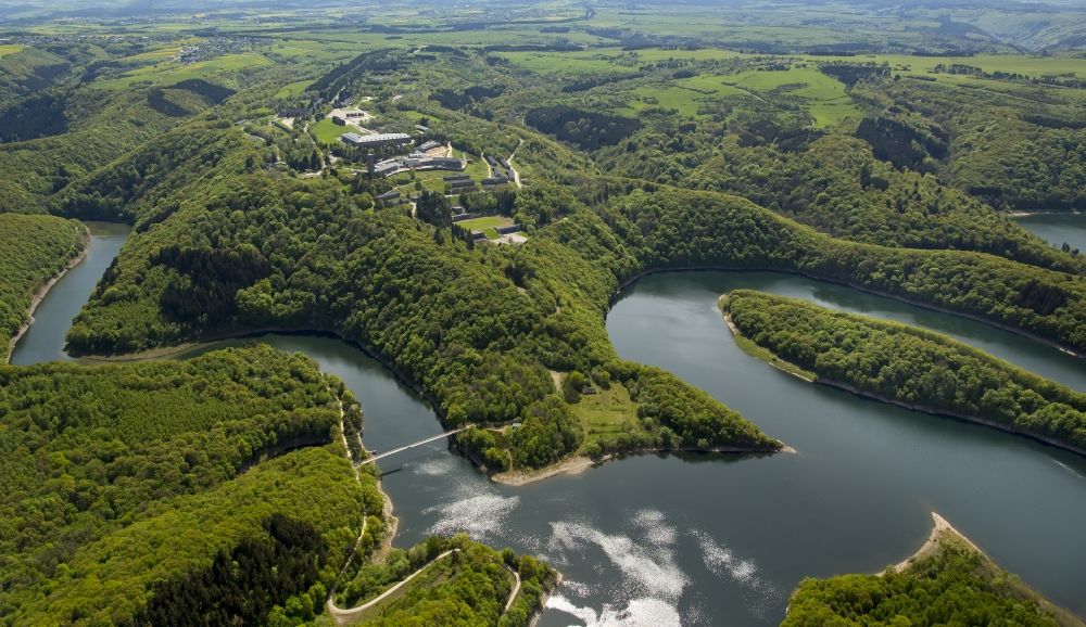 Aerial photograph Schleiden - Dam and shore areas at the lake Urfttalsperre near Schleiden in the state North Rhine-Westphalia. In view of the complex of buildings of the former Nazi Ordensburg Vogelsang, later barracks of the Belgian armed forces and today's Meeting Centre International Place in the Eifel National Park