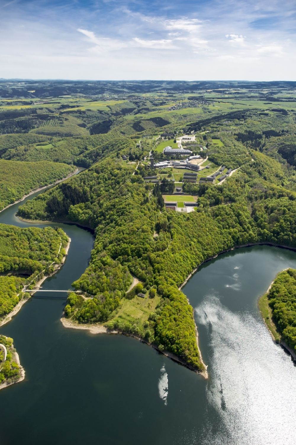 Aerial photograph Schleiden - Dam and shore areas at the lake Urfttalsperre near Schleiden in the state North Rhine-Westphalia. In view of the complex of buildings of the former Nazi Ordensburg Vogelsang, later barracks of the Belgian armed forces and today's Meeting Centre International Place in the Eifel National Park
