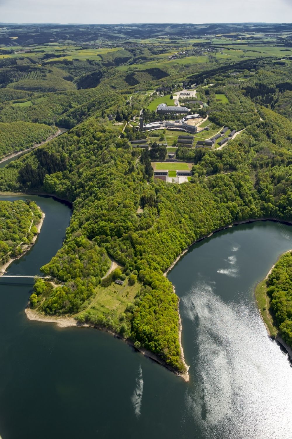 Schleiden from above - Dam and shore areas at the lake Urfttalsperre near Schleiden in the state North Rhine-Westphalia. In view of the complex of buildings of the former Nazi Ordensburg Vogelsang, later barracks of the Belgian armed forces and today's Meeting Centre International Place in the Eifel National Park