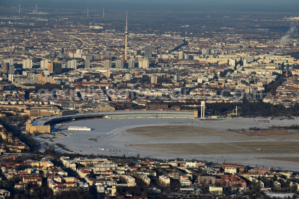 Aerial photograph Berlin - Wintry snowy premises of the former airport Berlin-Tempelhof Tempelhofer Freiheit in the Tempelhof part of Berlin, Germany. The premises include the historic main building and radar tower as well as two runways. Its hangars are partly used as refugee and asylum seekers accommodations