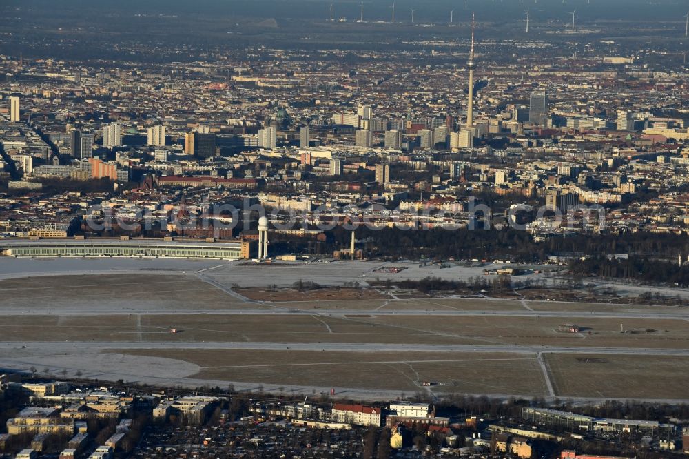 Aerial image Berlin - Wintry snowy premises of the former airport Berlin-Tempelhof Tempelhofer Freiheit in the Tempelhof part of Berlin, Germany. The premises include the historic main building and radar tower as well as two runways. Its hangars are partly used as refugee and asylum seekers accommodations