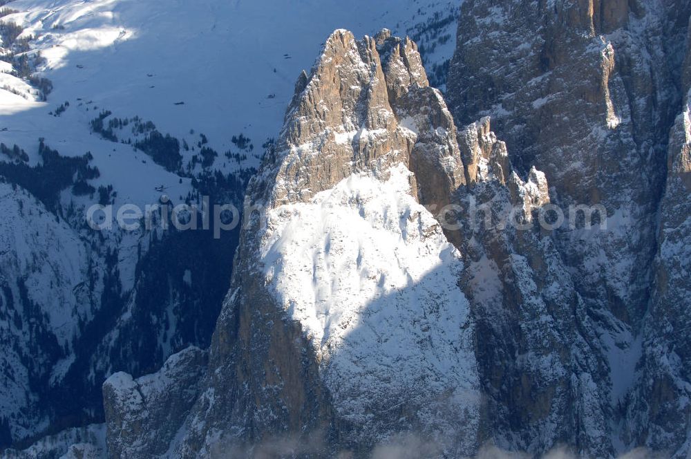 SEIS from above - Winterlich verschneite Seiser Alm mit dem Schlern Gebirgsmassiv der Dolomiten. Der Schlern (2.563 m, ital. Sciliar) ist ein Berg in den Dolomiten/Alpen in Südtirol, Italien. Trotz seiner geringen Höhe gilt er u.a. auf Grund seiner charakteristischen Form mit den beiden vorgelagerten Bergspitzen, der Santner- (2.413 m s.l.m.) und der Euringerspitze (2.394 m s.l.m.), als Wahrzeichen Südtirols. An den Schlern angelehnt ist die Seiser Alm, die höchstgelegene Hochweide Europas. 1974 wurde das umgebende Gebiet zum Naturpark erklärt, heute Teil des Naturparks Schlern-Rosengarten.Das Schlern-Massiv entstand wie die übrigen Berge der Dolomiten gegen Ende des Erdaltertums, in der sog. Permzeit. In der Tethys, die damals diese Landmassen bedeckte, sanken während einer langen Zeitspanne Ablagerungen von kleinen kalkhaltigen Tieren auf den Grund. Temperatur- und Lichtverhältnisse waren wahrscheinlich die Ursache, dass sich Korallenriffe ansiedelten. So bauten sich im Lauf von Jahrmillionen riesige Korallenbauten von tausenden Metern auf. Druck verdichtete langsam das Kalkgebilde. Durch Absinken der darunter liegenden Bozner Quarzporphyrplatte bildete sich die typische Form des Schlerns. Dann, zu Beginn des Erdmittelalters, erhob sich das Gebiet aus der Tethys. Die Afrikanische Platte schob sich langsam unter die Eurasische Platte und die Alpen falteten sich auf. Durch Erosion erlangte der Schlern schließlich sein heutiges Gesicht.