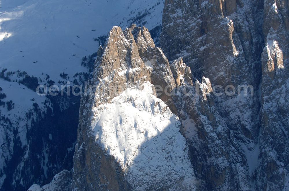 Aerial photograph SEIS - Winterlich verschneite Seiser Alm mit dem Schlern Gebirgsmassiv der Dolomiten. Der Schlern (2.563 m, ital. Sciliar) ist ein Berg in den Dolomiten/Alpen in Südtirol, Italien. Trotz seiner geringen Höhe gilt er u.a. auf Grund seiner charakteristischen Form mit den beiden vorgelagerten Bergspitzen, der Santner- (2.413 m s.l.m.) und der Euringerspitze (2.394 m s.l.m.), als Wahrzeichen Südtirols. An den Schlern angelehnt ist die Seiser Alm, die höchstgelegene Hochweide Europas. 1974 wurde das umgebende Gebiet zum Naturpark erklärt, heute Teil des Naturparks Schlern-Rosengarten.Das Schlern-Massiv entstand wie die übrigen Berge der Dolomiten gegen Ende des Erdaltertums, in der sog. Permzeit. In der Tethys, die damals diese Landmassen bedeckte, sanken während einer langen Zeitspanne Ablagerungen von kleinen kalkhaltigen Tieren auf den Grund. Temperatur- und Lichtverhältnisse waren wahrscheinlich die Ursache, dass sich Korallenriffe ansiedelten. So bauten sich im Lauf von Jahrmillionen riesige Korallenbauten von tausenden Metern auf. Druck verdichtete langsam das Kalkgebilde. Durch Absinken der darunter liegenden Bozner Quarzporphyrplatte bildete sich die typische Form des Schlerns. Dann, zu Beginn des Erdmittelalters, erhob sich das Gebiet aus der Tethys. Die Afrikanische Platte schob sich langsam unter die Eurasische Platte und die Alpen falteten sich auf. Durch Erosion erlangte der Schlern schließlich sein heutiges Gesicht.