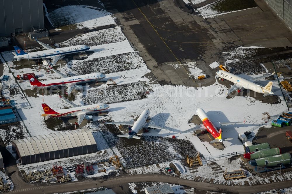 Aerial photograph Hamburg - Wintry snowy due to the pandemic, new aircraft A320 - A321 in the respective customer liveries parked in the open spaces and parking positions in the Airbus SE shipyard premises in the Finkenwerder district in Hamburg, Germany
