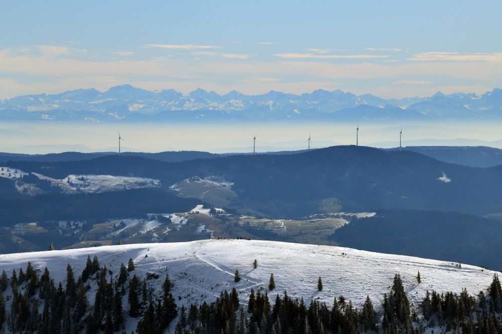 Aerial image Münstertal/Schwarzwald - Wintry snowy mountainous landscape of the mountain summit Belchen in the Black Forest in Muenstertal/Schwarzwald in the state Baden-Wurttemberg, Germany. Looking over the wind park Rohrenkopf with the 5 wind energy plants to the mountain range of the Alps