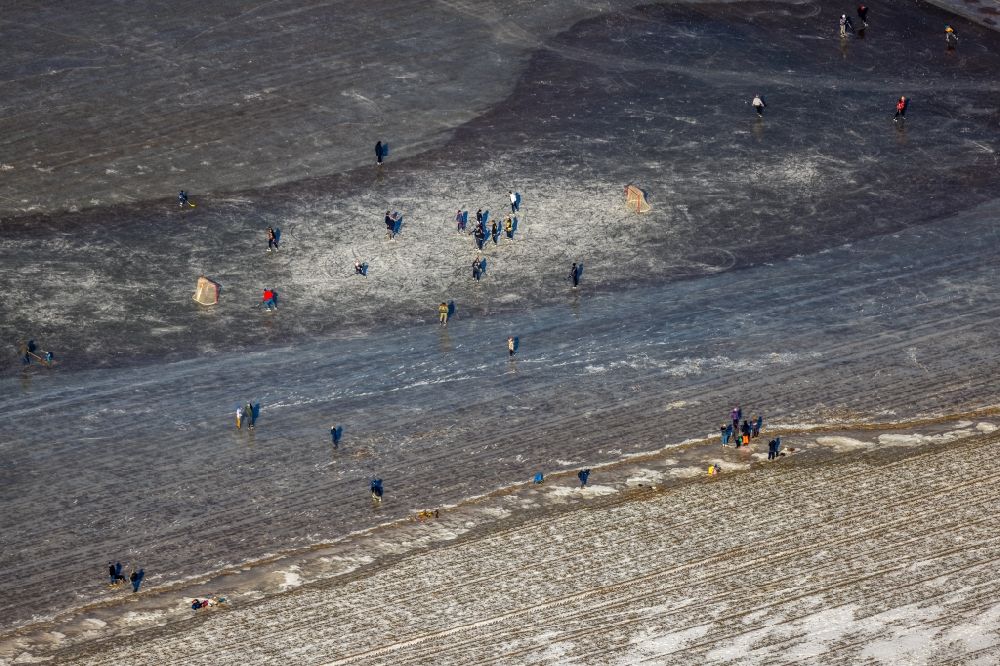 Duisburg from the bird's eye view: Wintry snowy view of walkers and passers-by walk on the ice and play ice hockey on the frozen bank areas in the course of the river Rhine in the district Ehingen in Duisburg at Ruhrgebiet in the state North Rhine-Westphalia, Germany