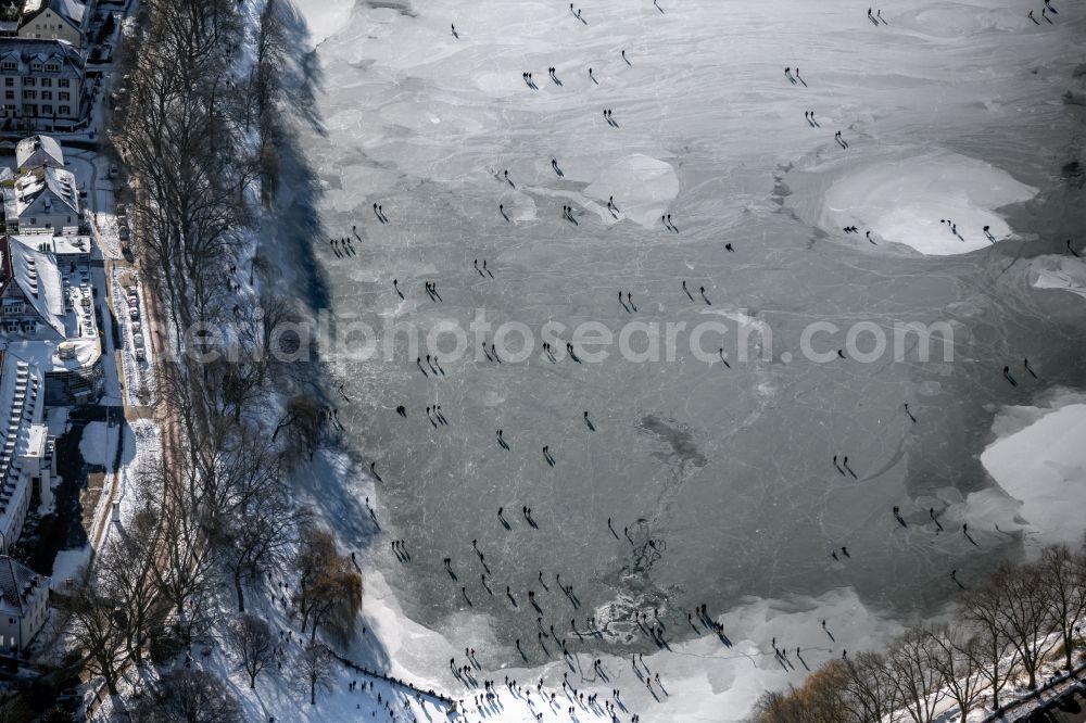 Münster from the bird's eye view: Wintry snowy strollers and passers-by walk on the ice sheet of the frozen bank areas of the lake - surface of Aasee in the district Pluggendorf in Muenster in the state North Rhine-Westphalia, Germany