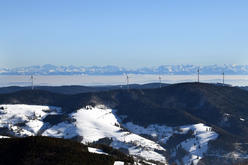 Aerial photograph Schopfheim - Wintry snowy landscape at the snow covered Rohrenkopf, the local mountain of Gersbach, a district of Schopfheim in Baden-Wuerttemberg. Wind turbines produce renewable energy in the wind farm in the Black Forest. Looking over the mountains to the Swiss Alps