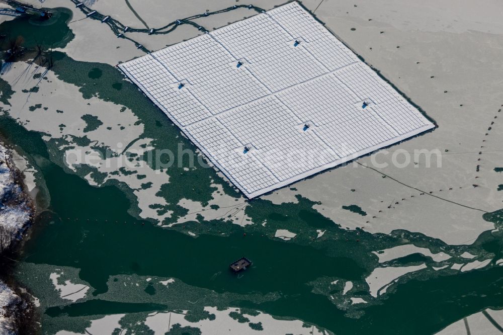 Dettelbach from the bird's eye view: Wintry snowy floating solar power plant and panels of photovoltaic systems on the surface of the water on Dettelbacher Baggersee in Dettelbach in the state Bavaria, Germany