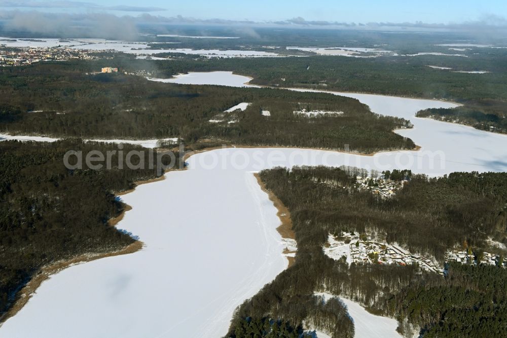 Templin from the bird's eye view: Wintry snowy riparian areas on the lake area of Luebbesee in a forest area in the district Ahrensdorf in Templin in the state Brandenburg, Germany