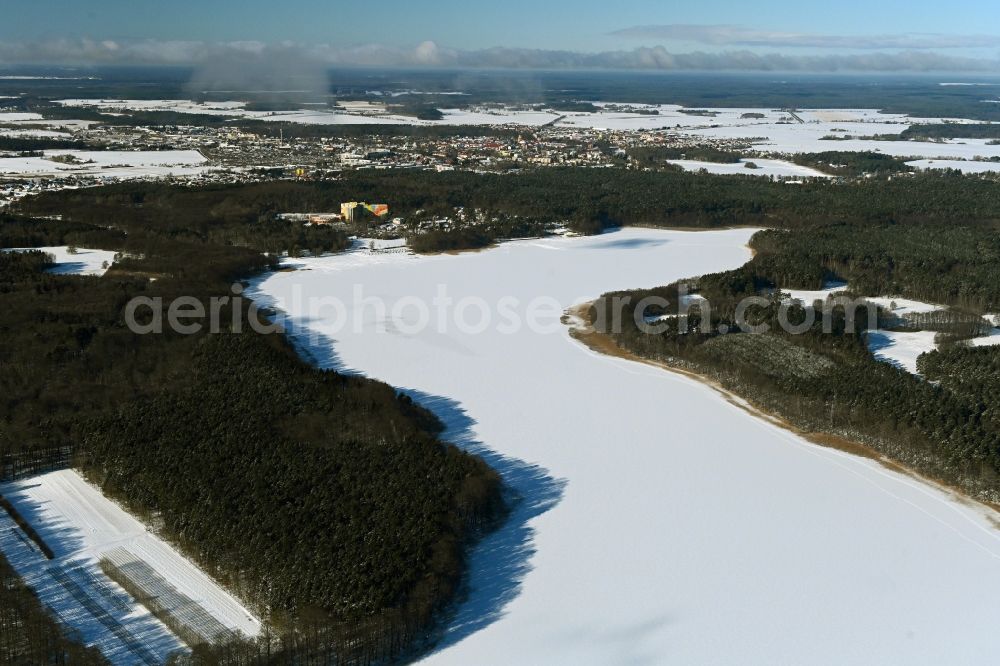 Templin from the bird's eye view: Wintry snowy riparian areas on the lake area of Luebbesee in a forest area in the district Ahrensdorf in Templin in the state Brandenburg, Germany